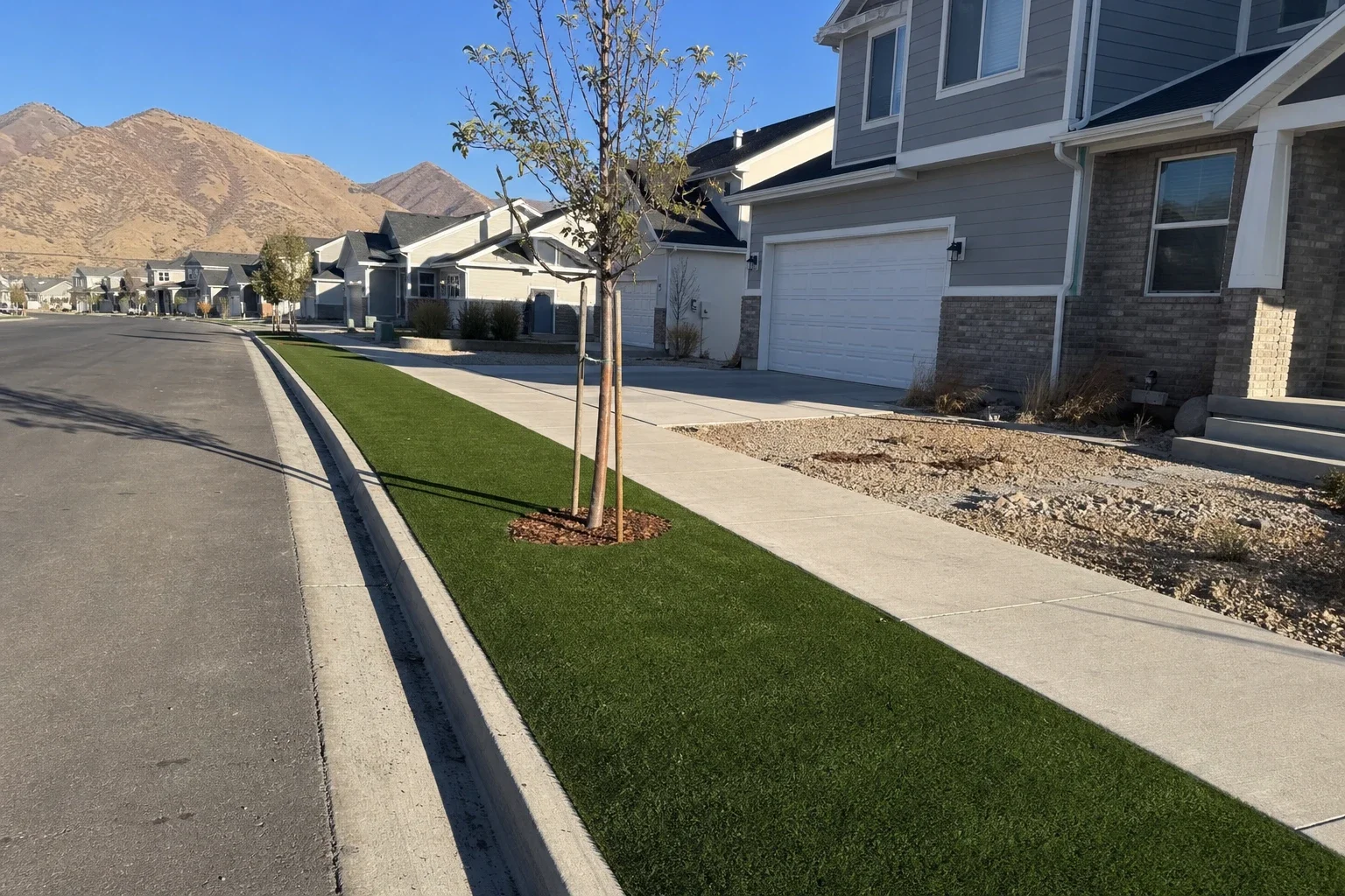 Artificial turf park strip running between the sidewalk and street on a Utah County block