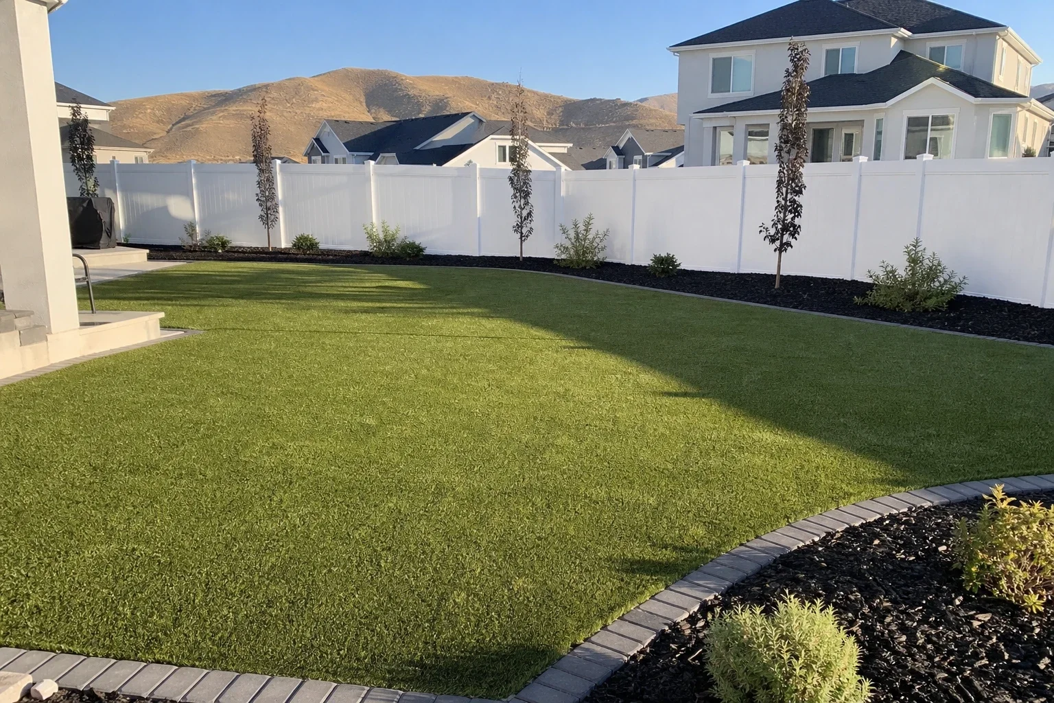 Artificial turf lawn filling a new-build Utah County backyard, edged with paver banding and dark mulch beds