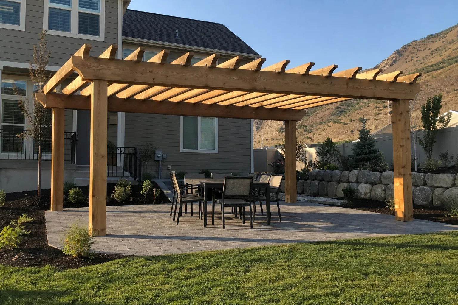 Finished cedar pergola over a paver patio and dining set in a Utah County backyard, with a stacked-stone retaining wall and the foothills behind