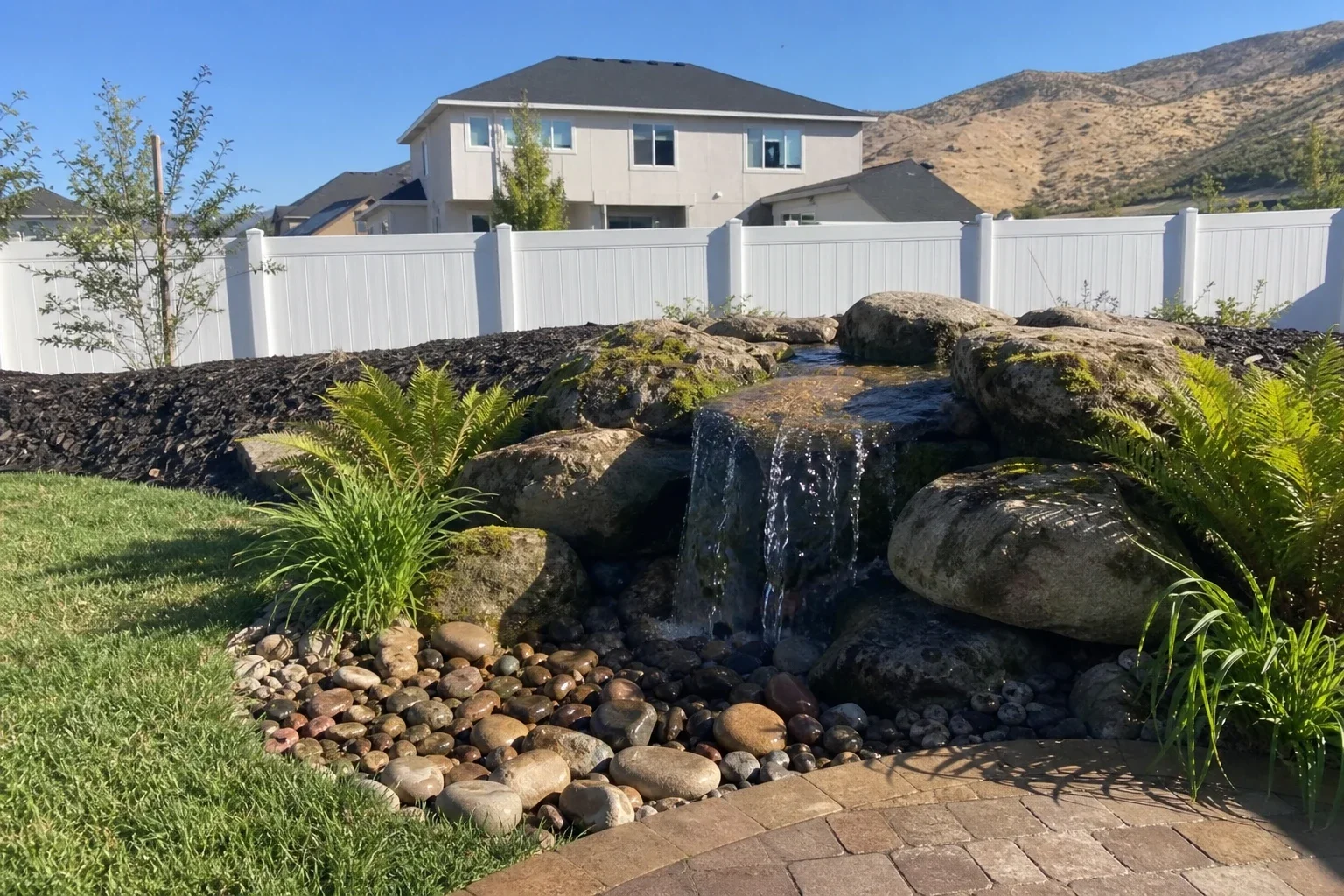 Pondless waterfall spilling over stacked boulders into a river-rock basin beside a paver patio